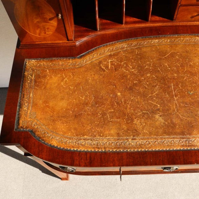 Vintage teak British mid-century desk with richly grained wood and worn leather top featuring detailed embossing and brass.