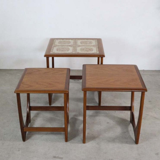 Set of three vintage teak G-Plan mid-century British nest tables with tile inlay on top table, showcasing rich wood grain.