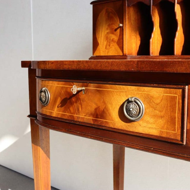 Vintage British mid-century teak desk with curved front drawer, decorative wood grain, brass ring handles, and slender.