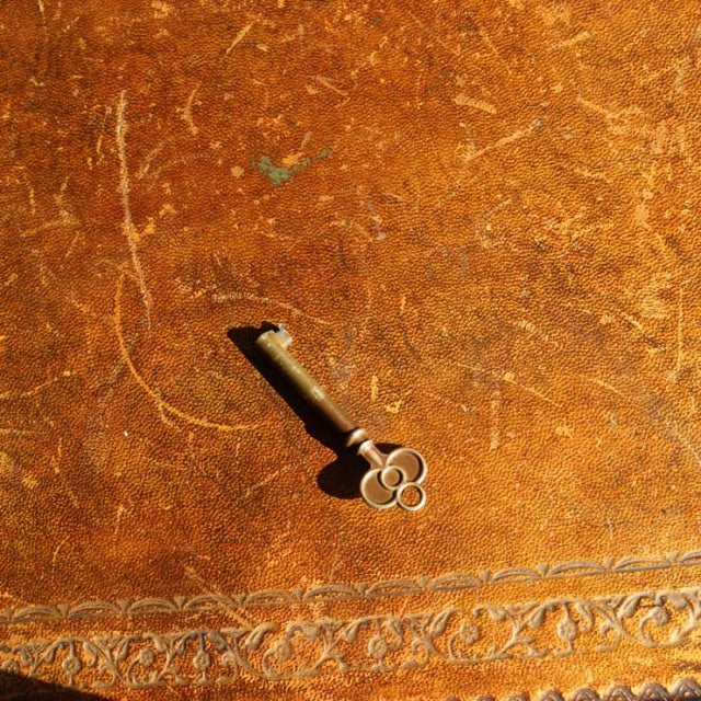 Close-up of vintage teak wood desk surface with intricate carved border and an antique brass key casting a shadow.