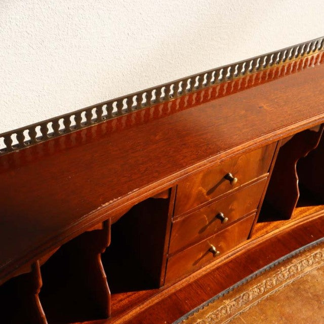 Vintage teak British mid-century desk with rich wood grain, brass gallery rail, and three central drawers flanked by open.
