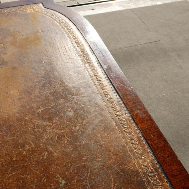 Close-up of vintage British mid-century teak desk surface with worn leather inlay and decorative embossed border detailing.