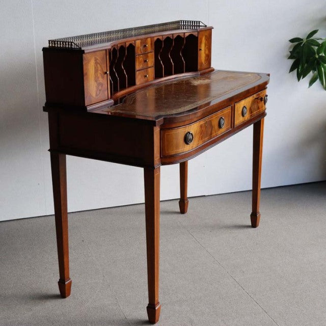 Vintage British mid-century teak desk with curved front, tapered legs, and ornate wood grain detailing.