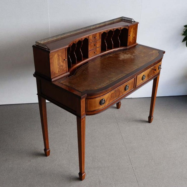 Vintage British mid-century teak writing desk with curved front, tapered legs, and rattan-backed pigeonholes.