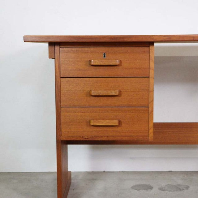 Mid-century vintage teak desk from Denmark with three drawers and visible wood grain, British-inspired design.