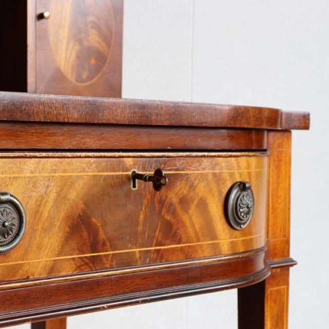 Vintage British mid-century teak desk with detailed wood grain, curved front drawer, and ornate metal keyhole and round.