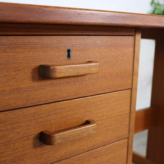 Mid-century vintage teak desk with smooth wood grain, two drawers with flush wooden handles, and British-Denmark design.