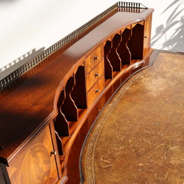 Vintage British teak mid-century desk with curved front, open compartments, brass gallery rail, and rich wood grain detailing.