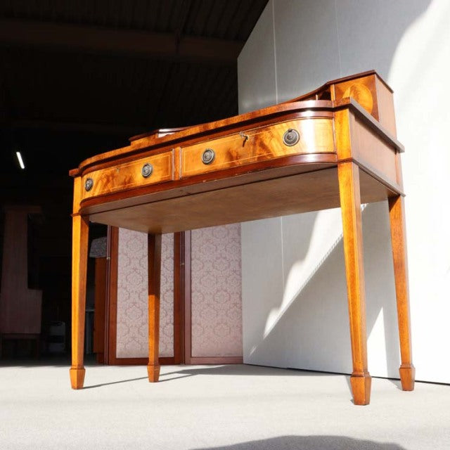 Mid-century British vintage teak desk with warm wood grain, tapered legs, and brass drawer pulls.