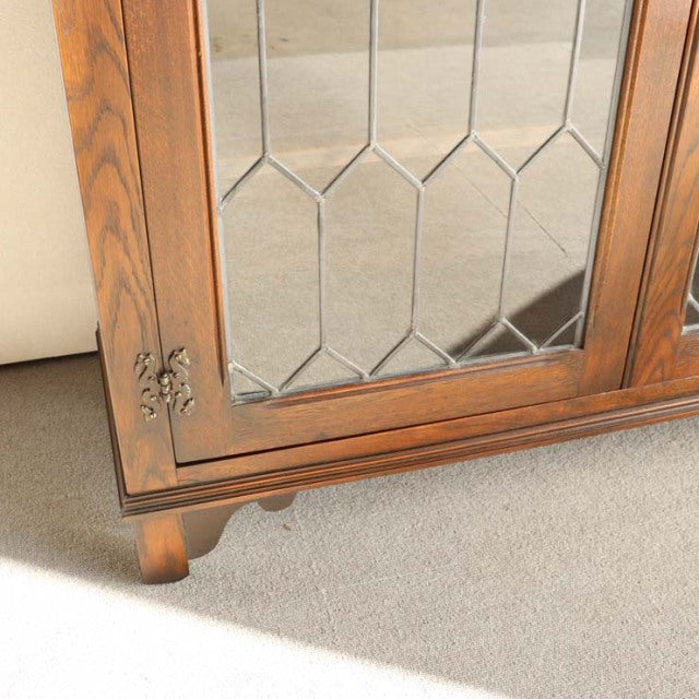 Mid-century British teak cabinet corner with ornate metal hinge, geometric leaded glass panel, and carved bracket feet.