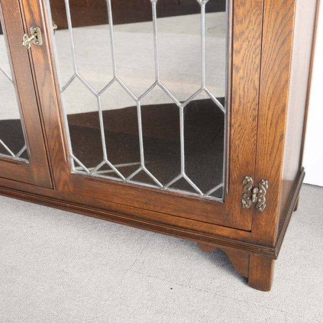 Vintage British mid-century teak cabinet with beveled glass panels and ornate brass hinges on sturdy square legs.