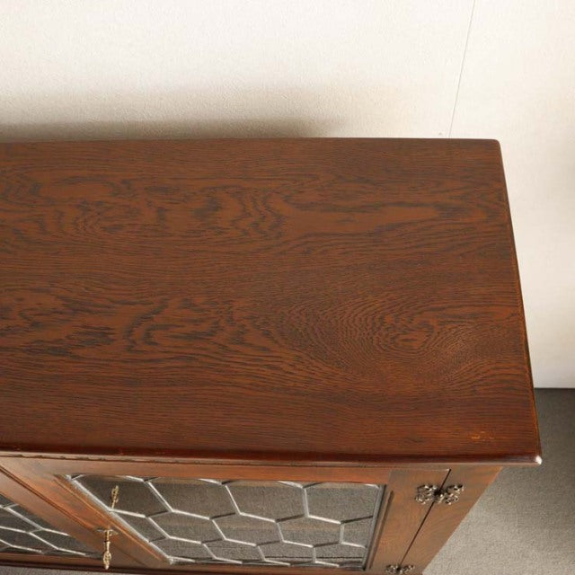 Mid-century British teak cabinet with rich wood grain, glass paneled doors, and slender tapered legs.