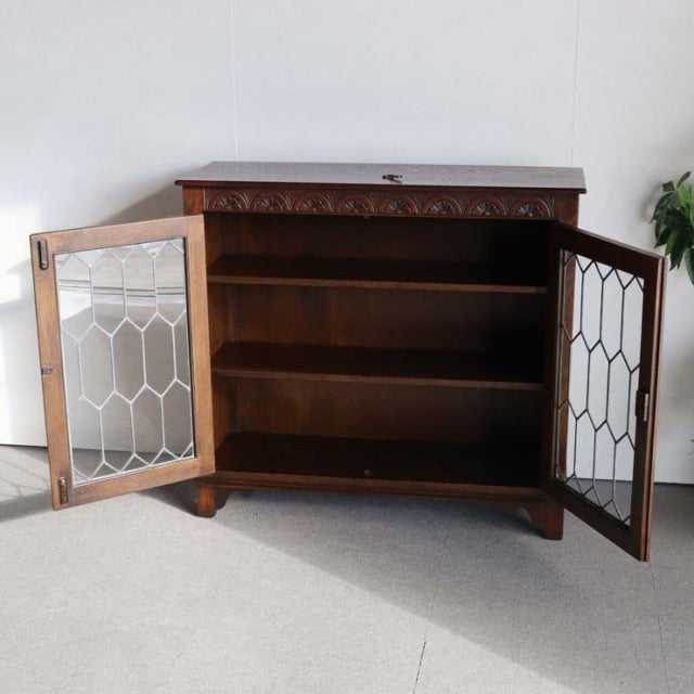 Vintage British mid-century teak cabinet with carved top edge, glass paneled doors, and tapered legs.