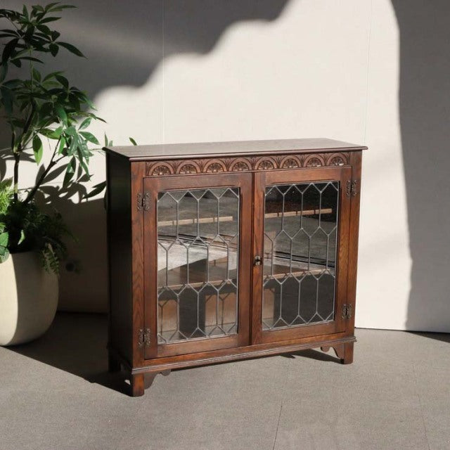 Vintage British teak cabinet by Jaycee with mid-century details, leaded glass doors, and intricate carved wood patterns,.
