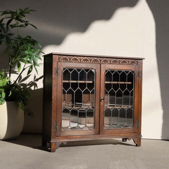 Vintage teak cabinet by Jaycee with British mid-century design, featuring intricate glass paneled doors and wood grain.