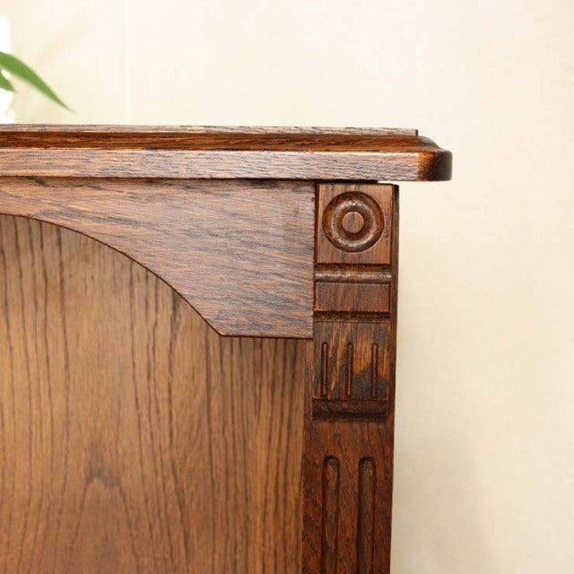 Close-up of vintage mid-century British oak cabinet corner with detailed wood grain and carved decorative accents.