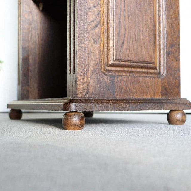Vintage British oak cabinet corner showcasing rich wood grain, detailed paneling, and rounded bun feet in mid-century style.
