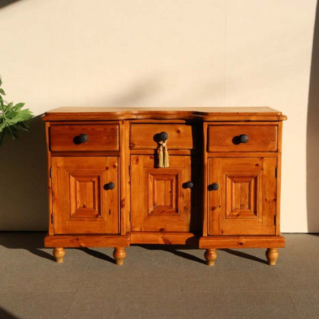 Vintage teak sideboard with rich wood grain, three drawers and cabinet doors, British mid-century design, turned legs, warm.
