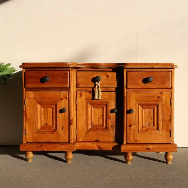 Vintage teak mid-century sideboard with rich wood grain, paneled doors, three drawers, and turned legs, British-Denmark.
