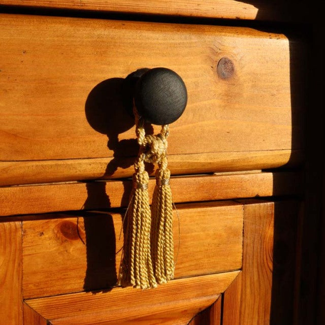 Close-up of vintage teak sideboard drawer with visible wood grain, dark round knob, and decorative golden tassels,.