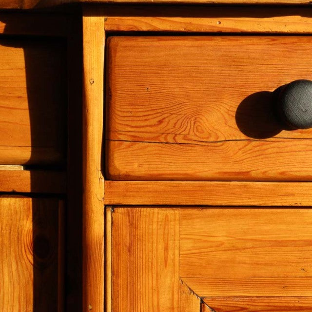 Close-up of vintage teak wood sideboard drawer front showing warm grain and rounded black knob, mid-century British design.