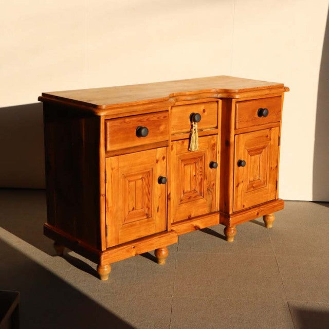 Vintage teak sideboard with mid-century British design, detailed wood grain, rounded legs, and three drawers and cabinets.