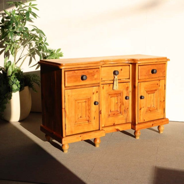 Vintage teak sideboard in British mid-century style with rich wood grain, three drawers, and paneled doors on turned legs.