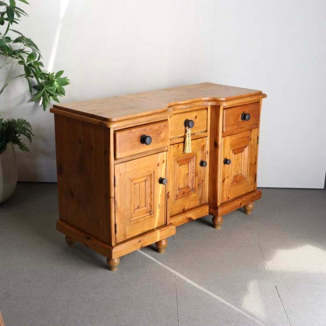 Vintage British mid-century teak sideboard with rich wood grain, paneled doors, round black knobs, and sturdy turned legs.