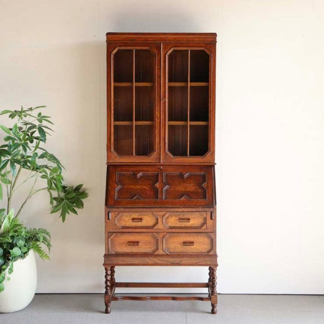 Vintage mid-century British teak cabinet with glass-paneled upper doors, intricate wood grain, ornate carved drawers, and.
