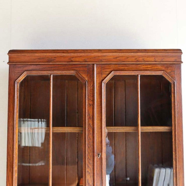 Vintage teak mid-century British cabinet from 1930s with rich wood grain, glass-paneled doors, and tapered legs.