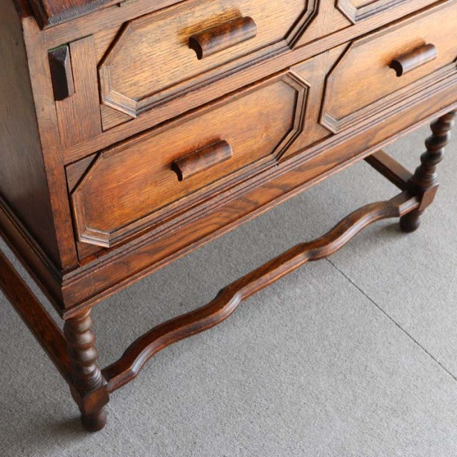 Vintage 1930s British teak cabinet with carved drawer fronts, turned legs, and wavy stretcher detail.