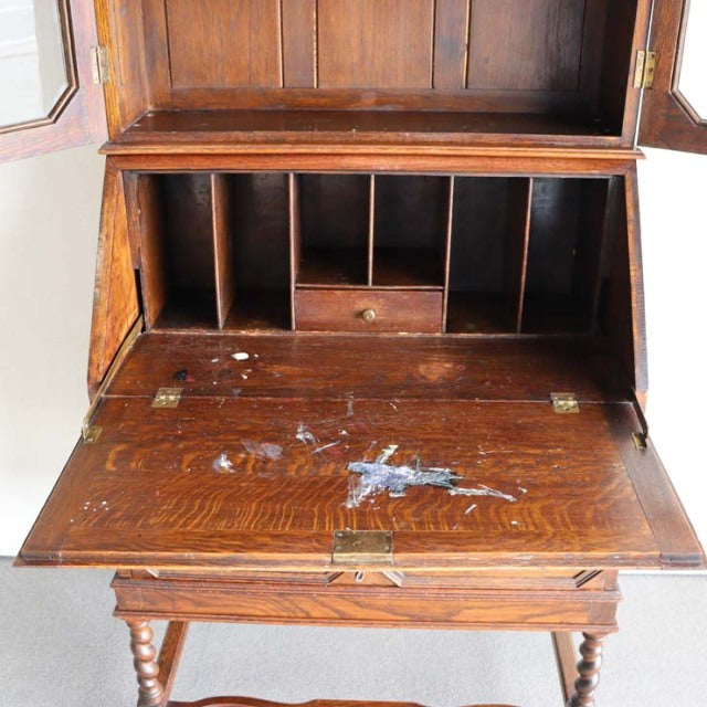 Vintage British teak writing cabinet from the 1930s with dark wood grain, drop-front desk, and turned legs in mid-century.