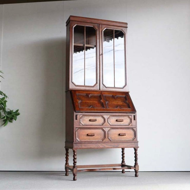 Vintage mid-century British teak cabinet with mirrored upper doors, angled drop-front desk, and turned legs.