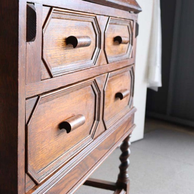 Vintage 1930s British teak cabinet with carved drawer fronts and turned legs, showcasing rich wood grain and mid-century.