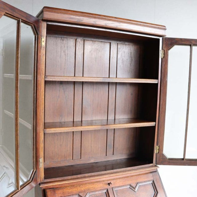 Vintage teak mid-century British cabinet with glass paneled double doors, rich wood grain, and sturdy tapered legs.