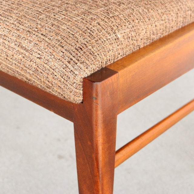 Close-up of mid-century McIntosh dining chair corner showcasing rich teak wood grain and textured beige fabric upholstery,.