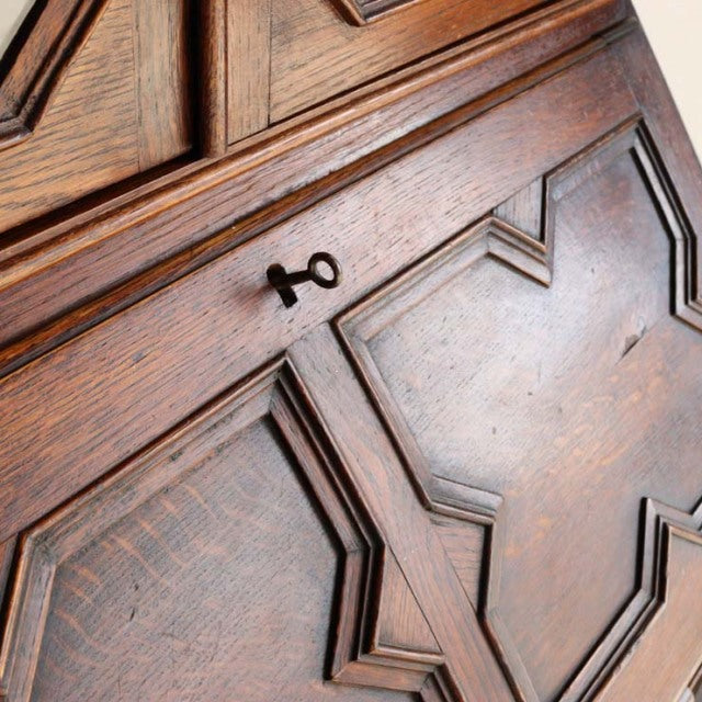 Vintage British mid-century teak cabinet with geometric carved panel doors and a small metal key, showcasing rich wood grain .