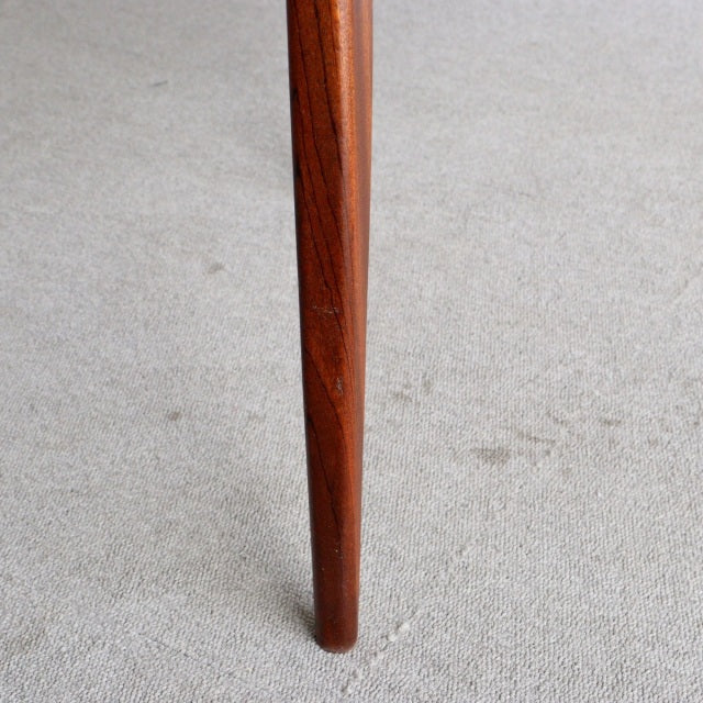 Tapered teak leg of vintage British mid-century McIntosh dining chair with rich wood grain and smooth finish on light carpet.