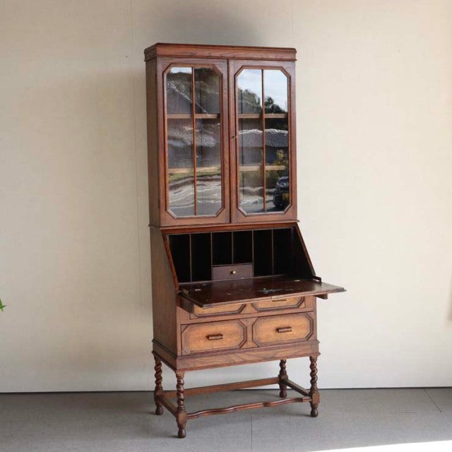 Vintage teak British mid-century cabinet with glass paneled doors, carved drawer fronts, and turned legs.