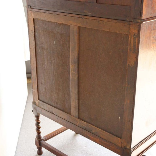 Vintage British teak cabinet from the 1930s with rich wood grain, paneled doors, and turned mid-century legs.
