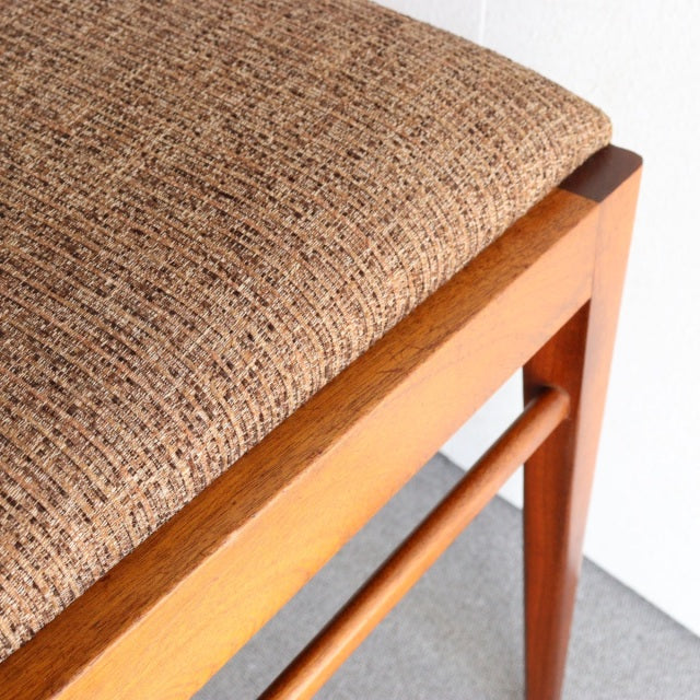 Vintage teak dining chair corner showing mid-century British design with textured brown fabric seat and smooth wood grain.