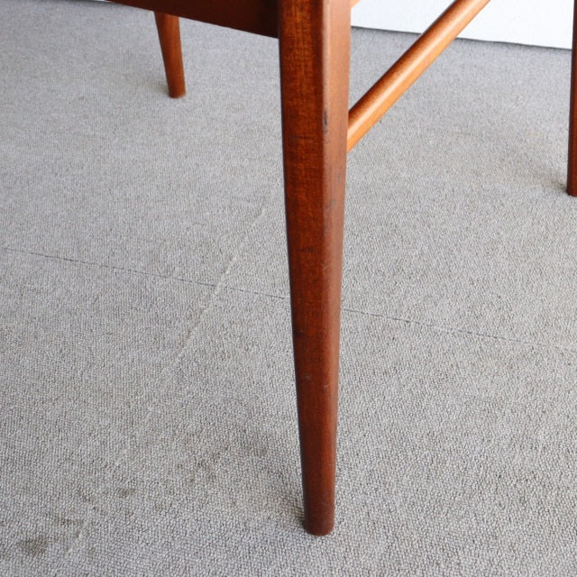 Tapered teak leg of vintage British mid-century McIntosh dining chair with warm wood grain and smooth finish on gray carpet.