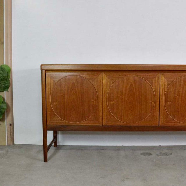 Mid-century British vintage teak sideboard by Nathan with geometric carved circular patterns on three cabinet doors, slender .