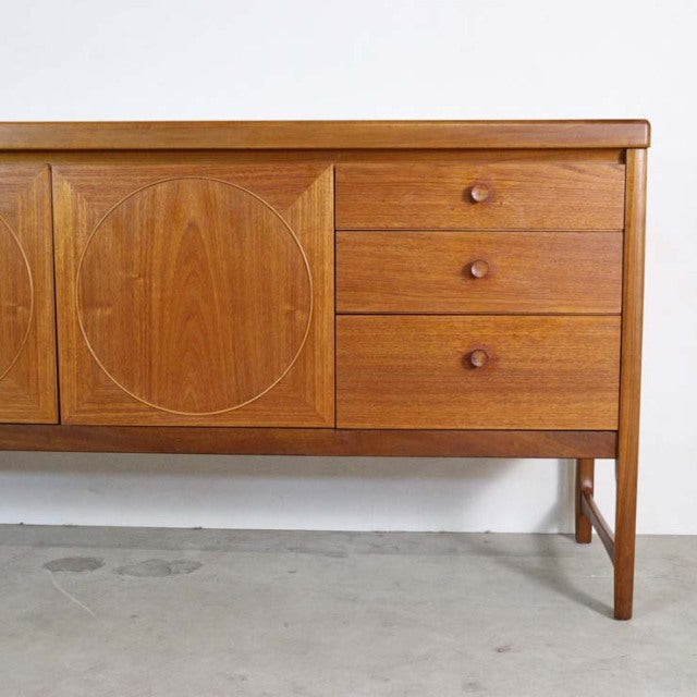 Vintage mid-century teak sideboard by British brand Nathan, featuring smooth wood grain, round door detail, three drawers,.