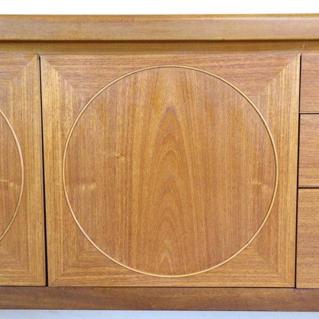 Close-up of vintage British mid-century teak sideboard door featuring circular inlay and rich wood grain.