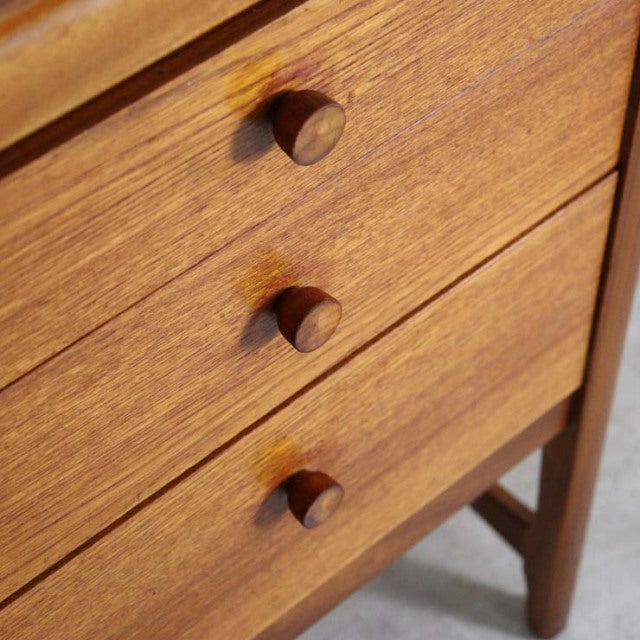 Close-up of vintage British mid-century teak sideboard drawers with round wooden knobs and visible grain.