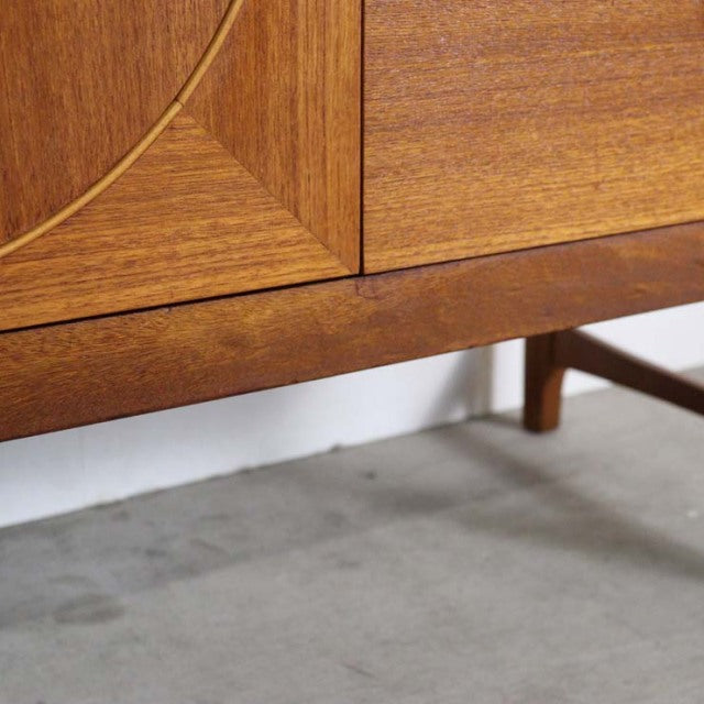Close-up of vintage teak sideboard corner showing rich wood grain, clean mid-century British design, and slender wooden legs .