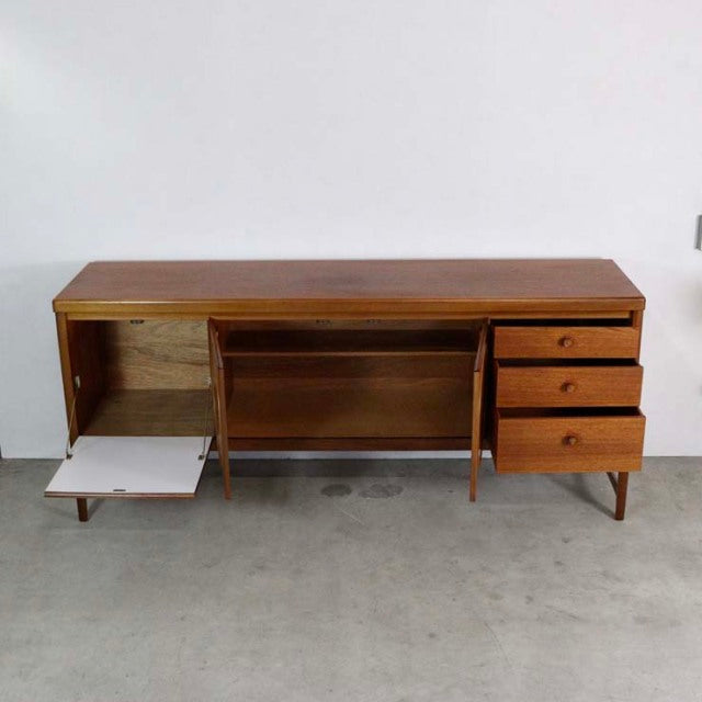 Vintage Nathan teak sideboard with mid-century British design, featuring three drawers, a drop-down door, and tapered legs,.