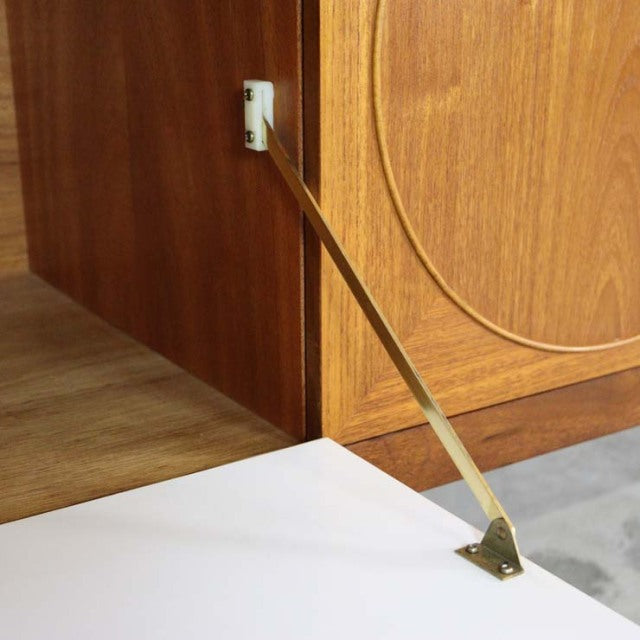Close-up of mid-century vintage teak sideboard door held open by brass support arm, showing rich wood grain and British.