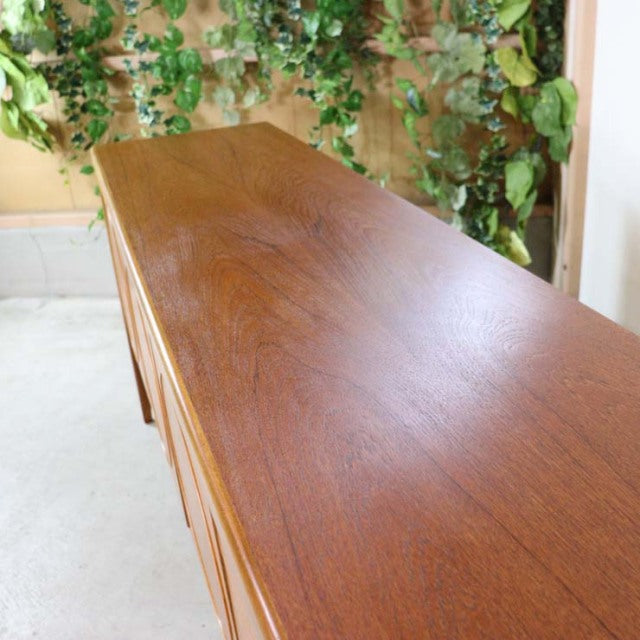 Mid-century British teak sideboard by Nathan with rich wood grain and sleek rectangular top against natural backdrop.